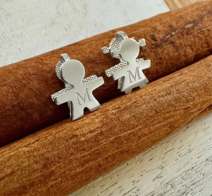 White-Gold pendants shaped like people with 'M' initials on a wooden surface