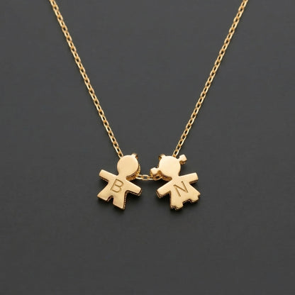 Gold necklace with two child-shaped pendants on a dark background with engraving initial.
