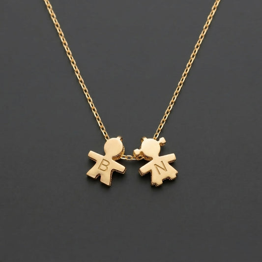 Gold necklace with two child-shaped pendants on a dark background with engraving initial.