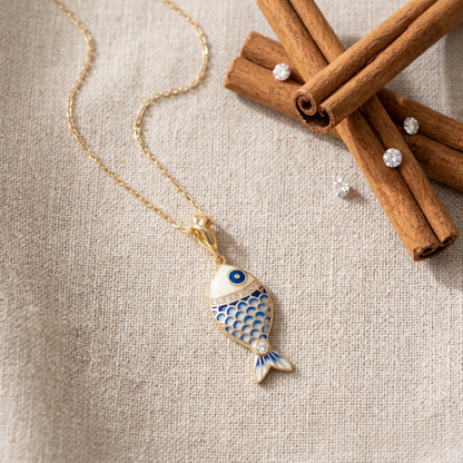Gold necklace with a fish pendant on a beige fabric background with cinnamon sticks.