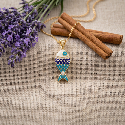 Gold necklace with a blue fish pendant on a textured fabric background with lavender and cinnamon sticks.
