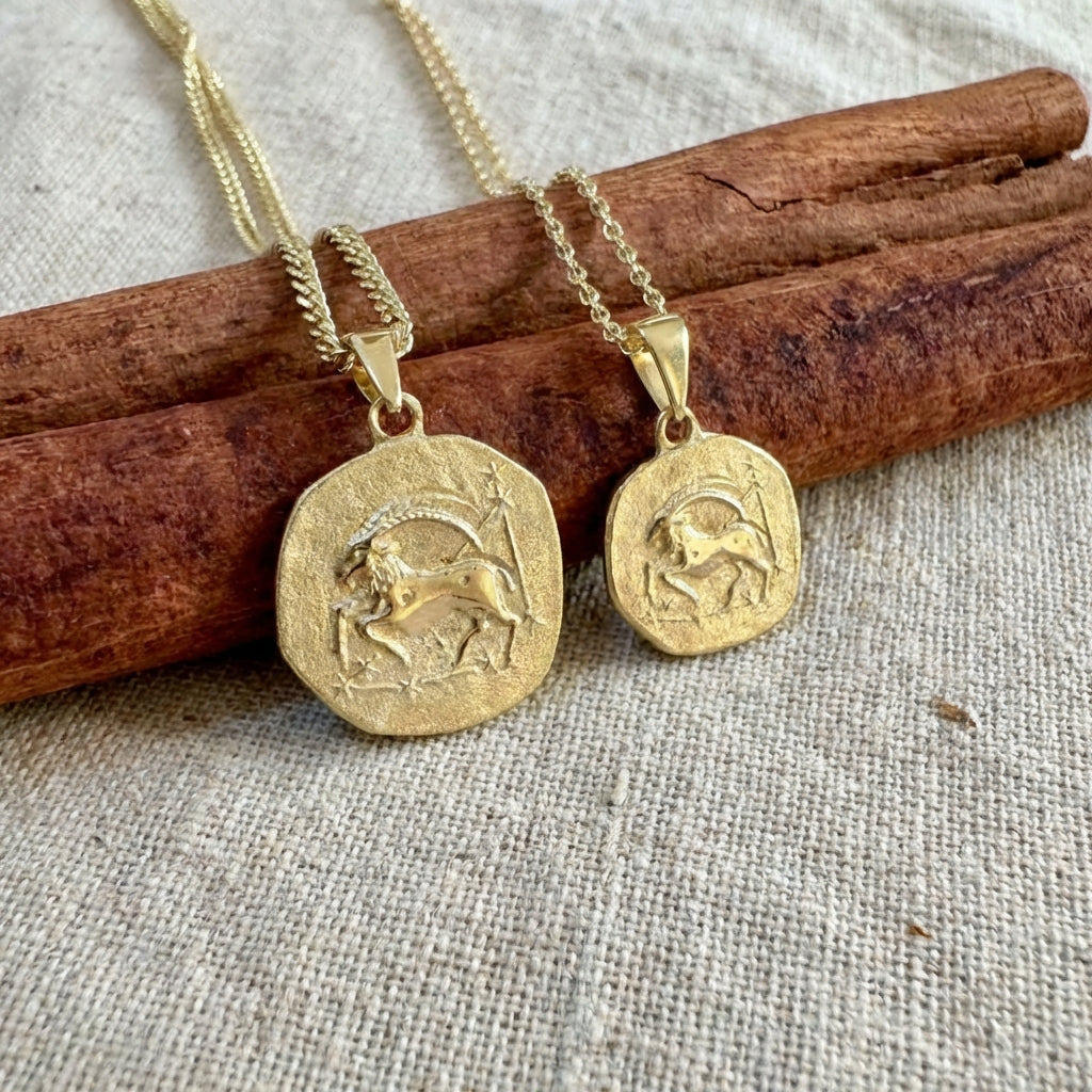 Two gold pendants on chains lying on cinnamon sticks with a textured fabric background