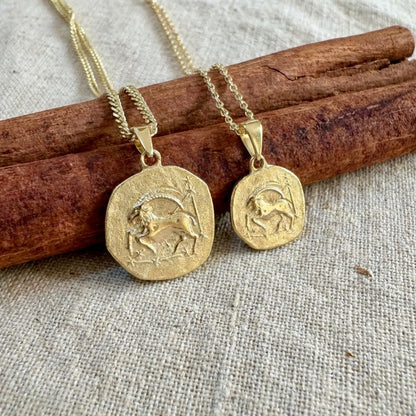 Two gold pendants on chains lying on cinnamon sticks with a textured fabric background