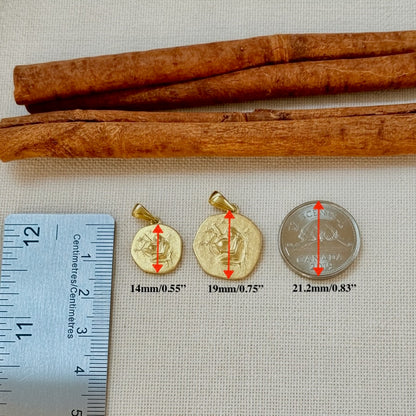 Three gold pendants and a silver coin with measurements relative to a ruler and cinnamon sticks on a textured surface.