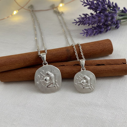 Two silver  zodiac pendants on chains with cinnamon sticks and lavender flowers in the background.