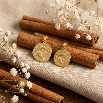 Gold pendants on cinnamon sticks with white flowers on a textured surface
