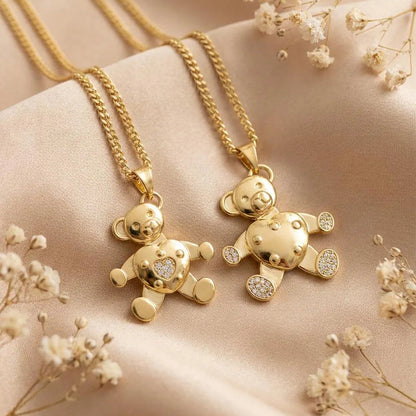 Two gold teddy bear pendants on chains with small flowers around on a beige fabric background.